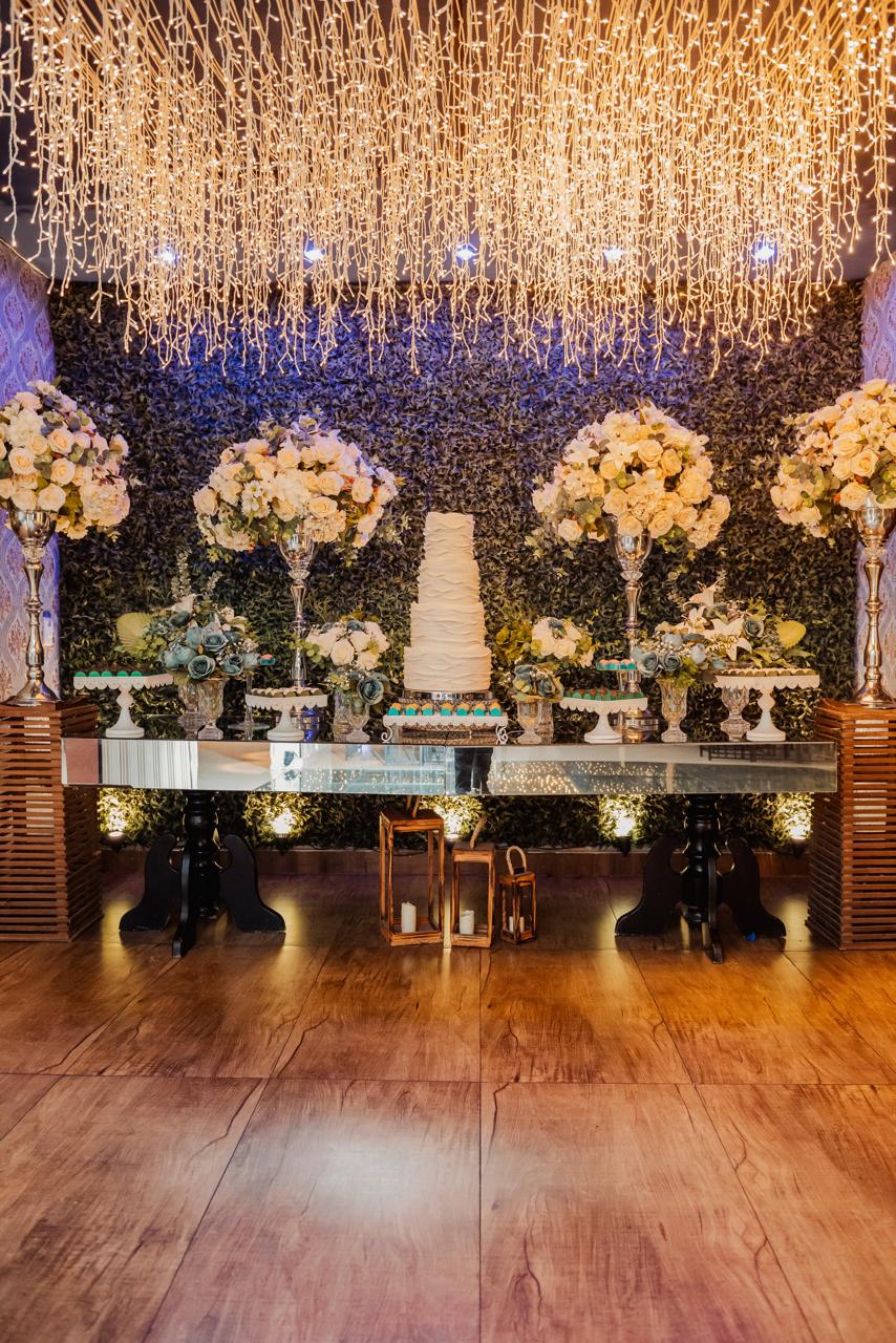 Mesa do bolo de casamento com cortina de luzes e flores no Buffet Dream Hall